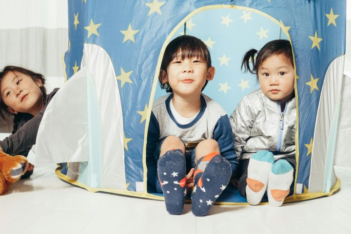 Three children sitting in a star-patterned tent enjoying playtime with toys.