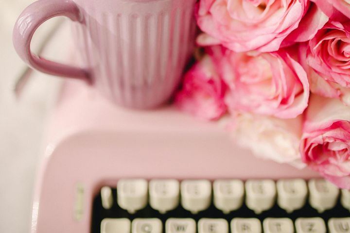 Aesthetic composition of pink roses, coffee mug, and vintage typewriter in soft pastel colors.