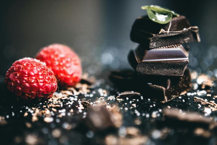 Artistic close-up of dark chocolate pieces with fresh raspberries, perfect for dessert visuals.